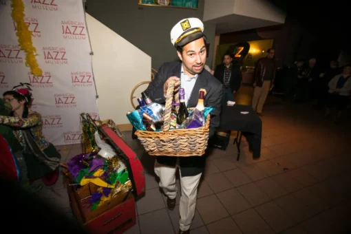A man with a captain's hat carrying a gift basket of alcoholic beverages.